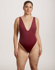 Woman wearing a burgundy swimsuit against a plain background