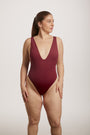Woman wearing a burgundy swimsuit against a plain background